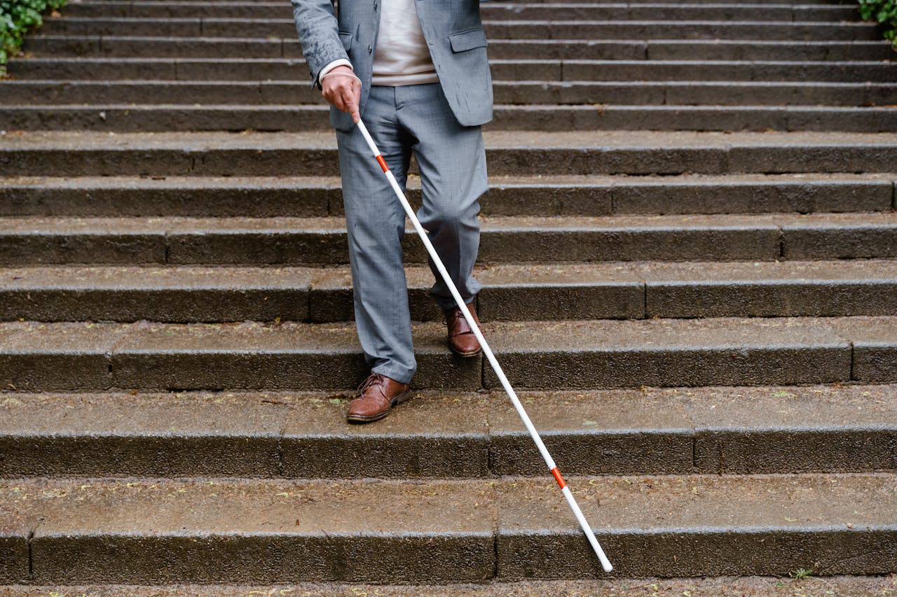 Man with visual impairment using white cane to walk down outdoor steps.