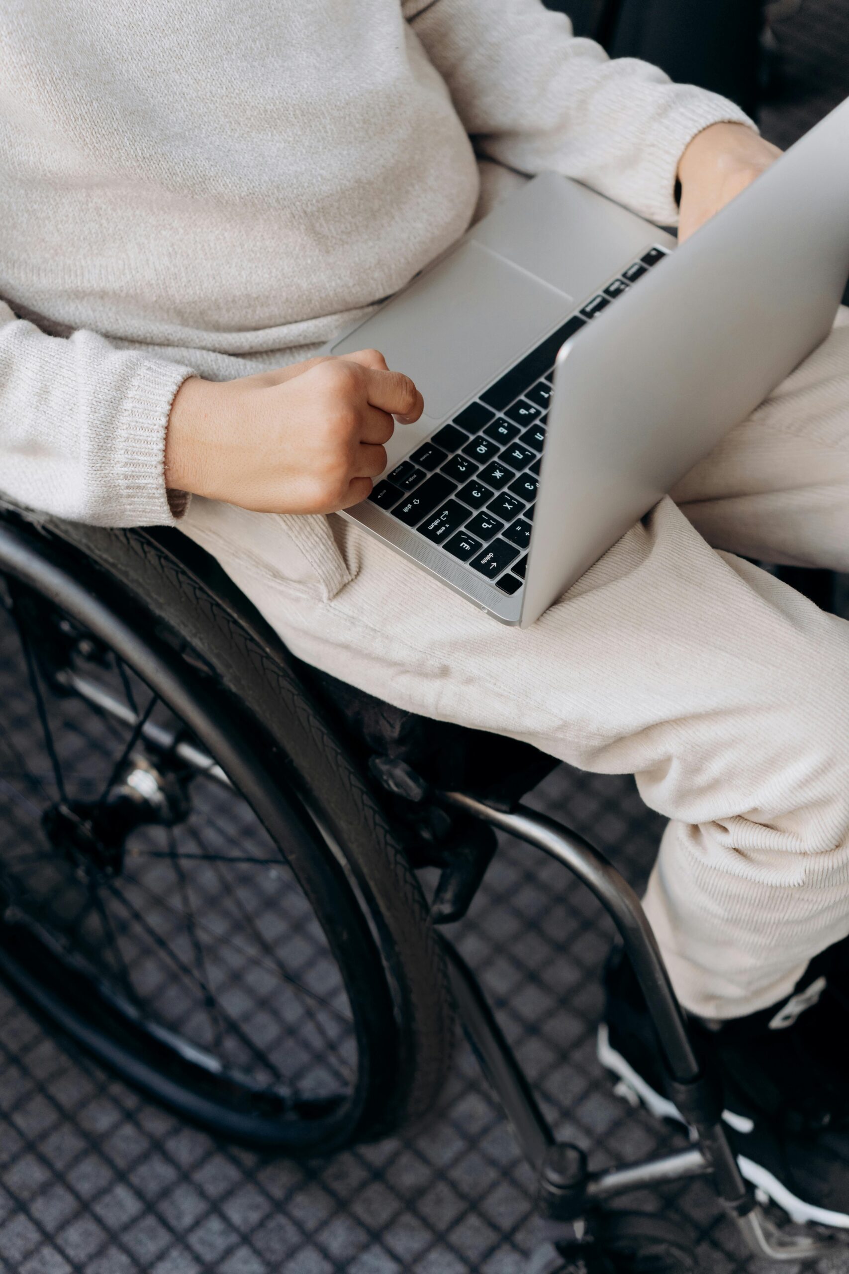 Close-up of an individual in a wheelchair using a laptop indoors, emphasizing technology and accessibility.